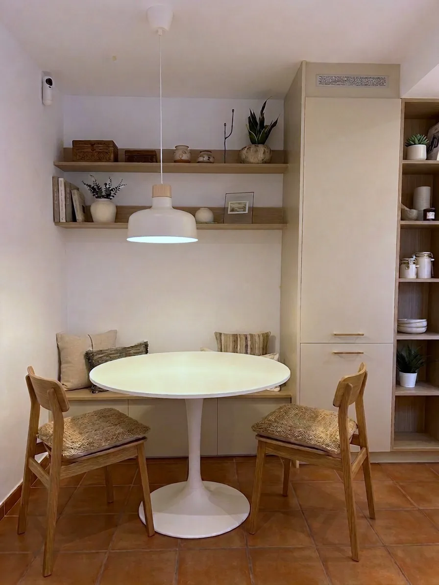 Rincón comedor con banco empotrado, mesa redonda blanca y estantes de madera