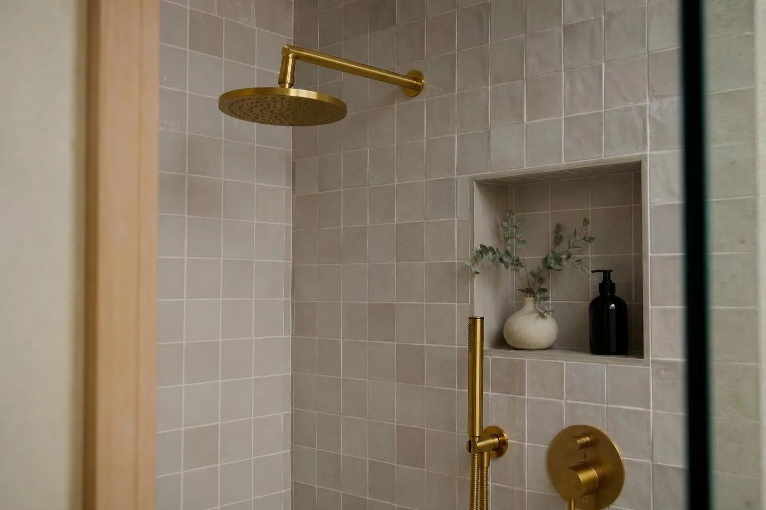 Detalle de grifería de ducha dorada sobre pared alicatada