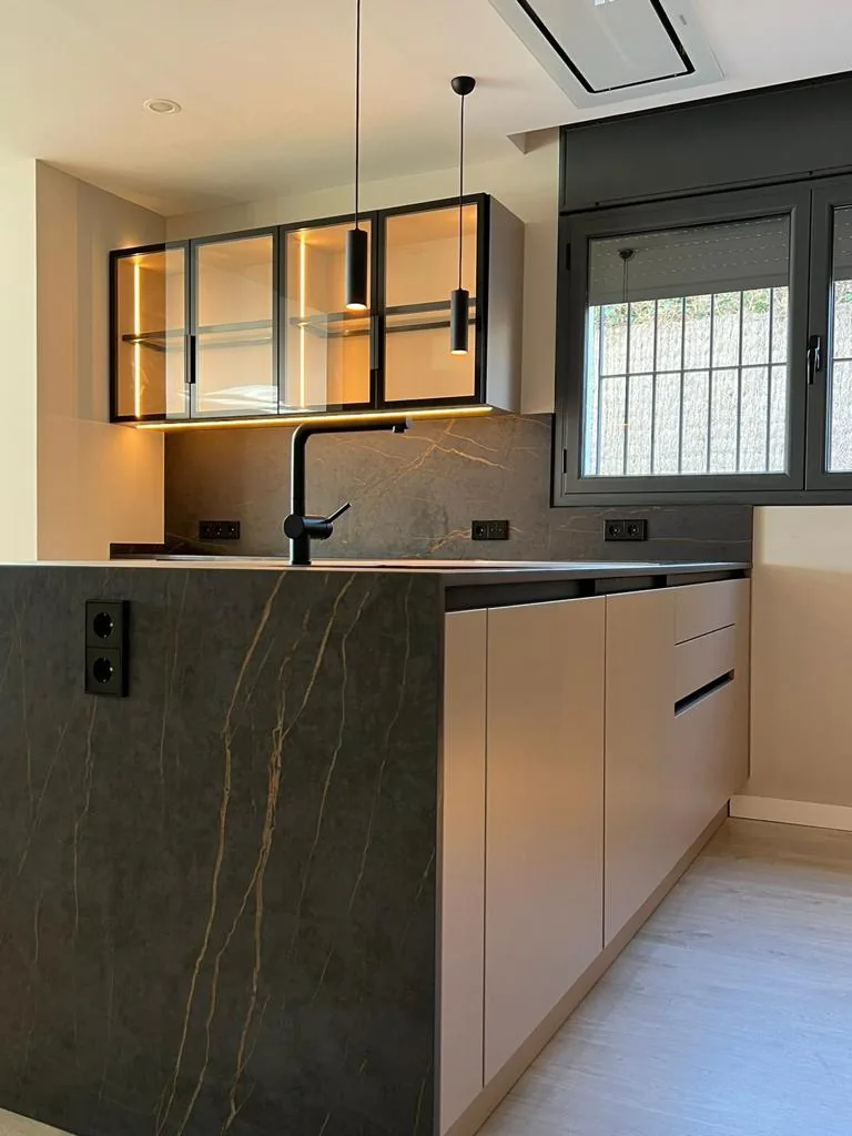 Península de cocina en piedra oscura con veta dorada y armarios altos de cristal