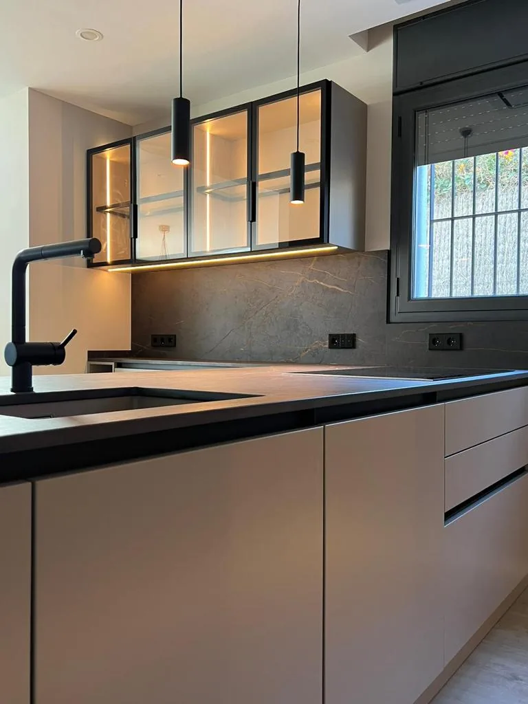 Cocina moderna con vitrinas de cristal y marco negro, grifo negro y encimera oscura