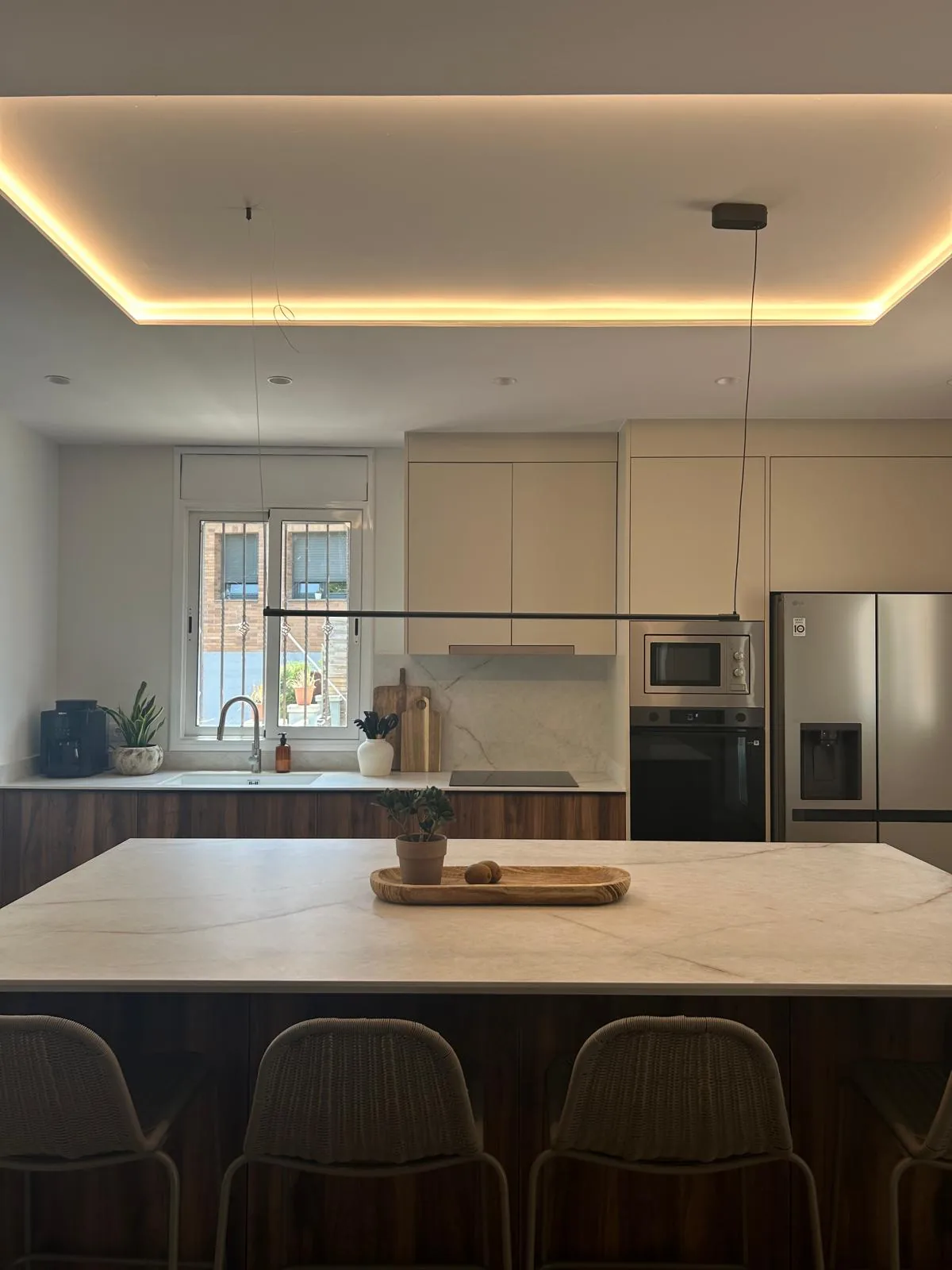 Cocina con isla central, taburetes y falso techo con iluminación led perimetral
