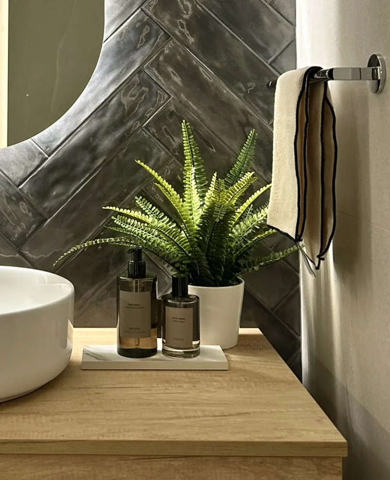 Detalle de baño con azulejo gris en espiga, lavabo sobre encimera y mueble de madera