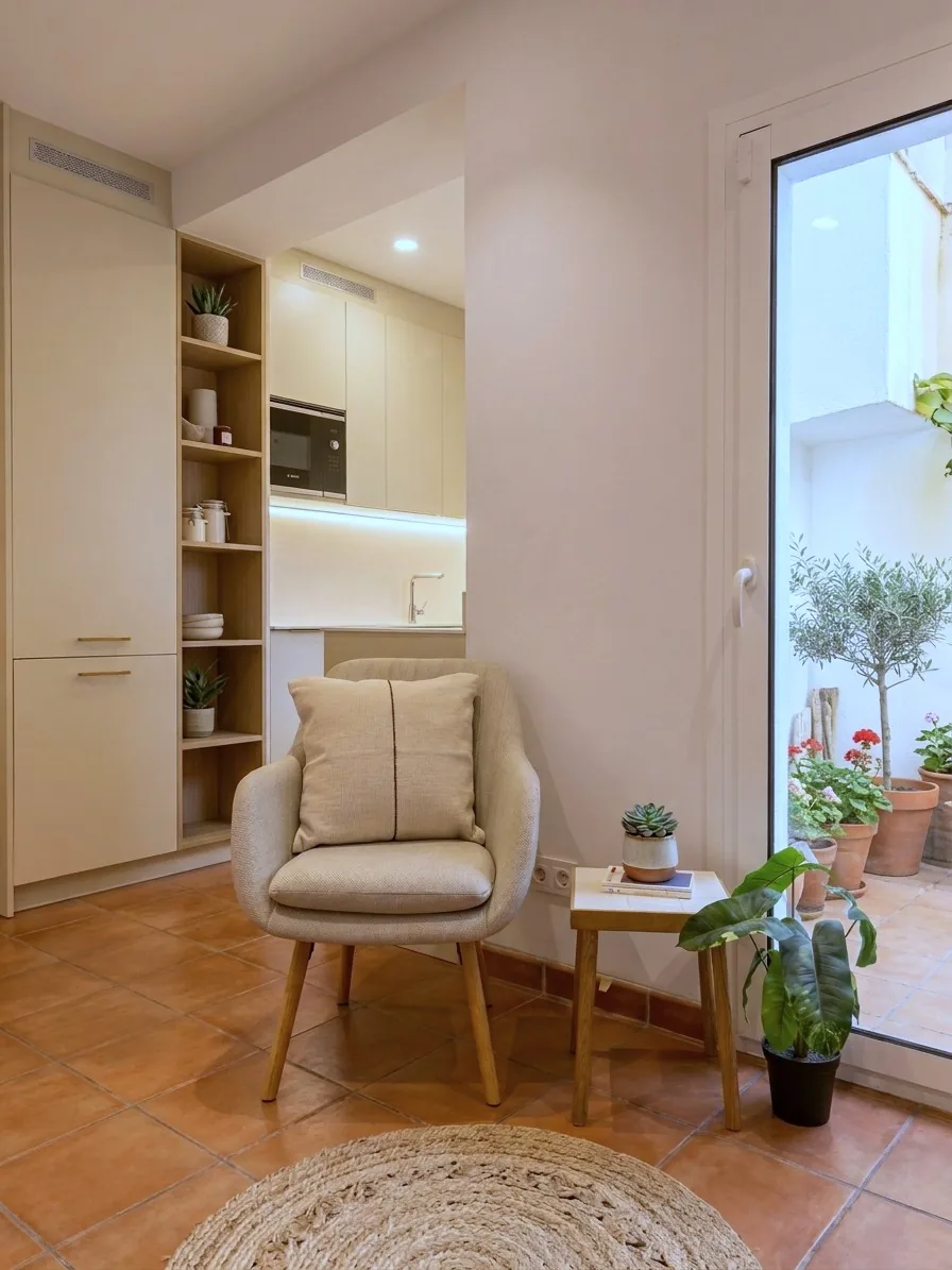 Salón con cocina integrada en armarios claros y estantes de madera, junto a un patio