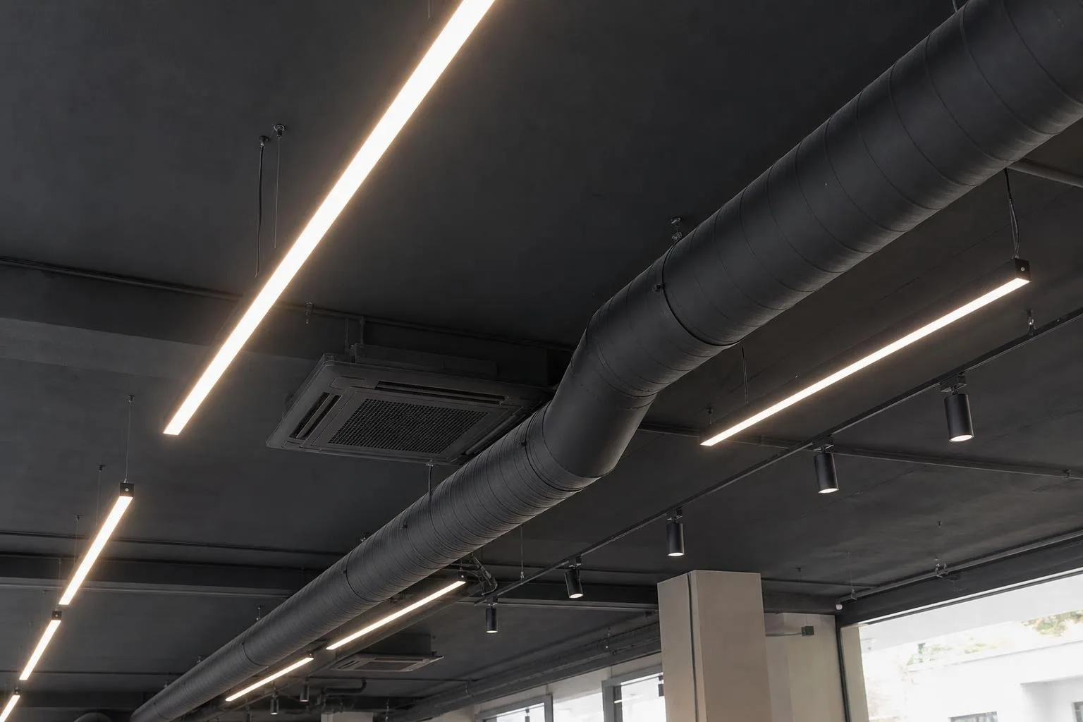 Techo de oficina pintado en oscuro con conductos vistos e iluminación lineal